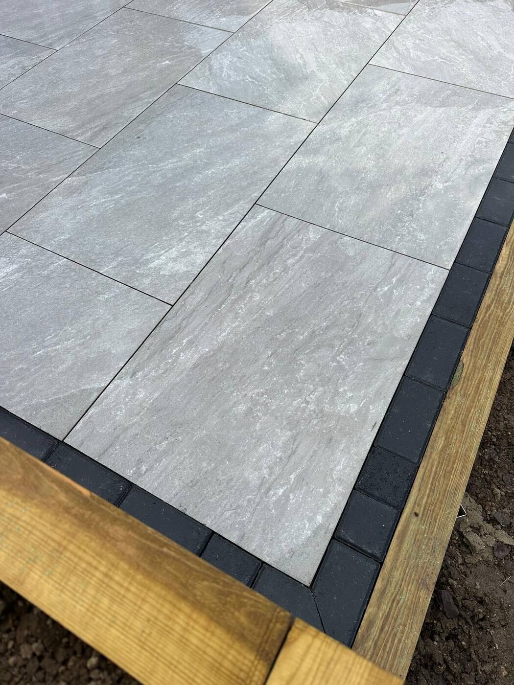 Porcelain patio with black trim edging against timber sleepers